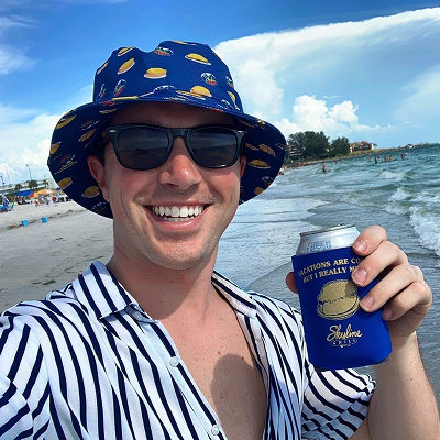 Man at beach wearing skyline bucket hat and holding a drink in a Skyline coozie